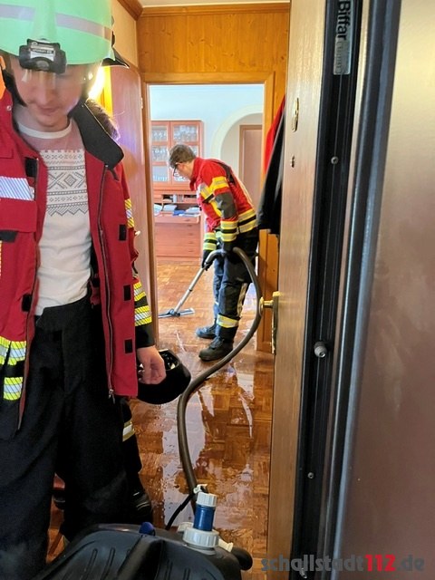 Feuerwehrangehörige nehmen Wasser in einem Wohnungsflur auf