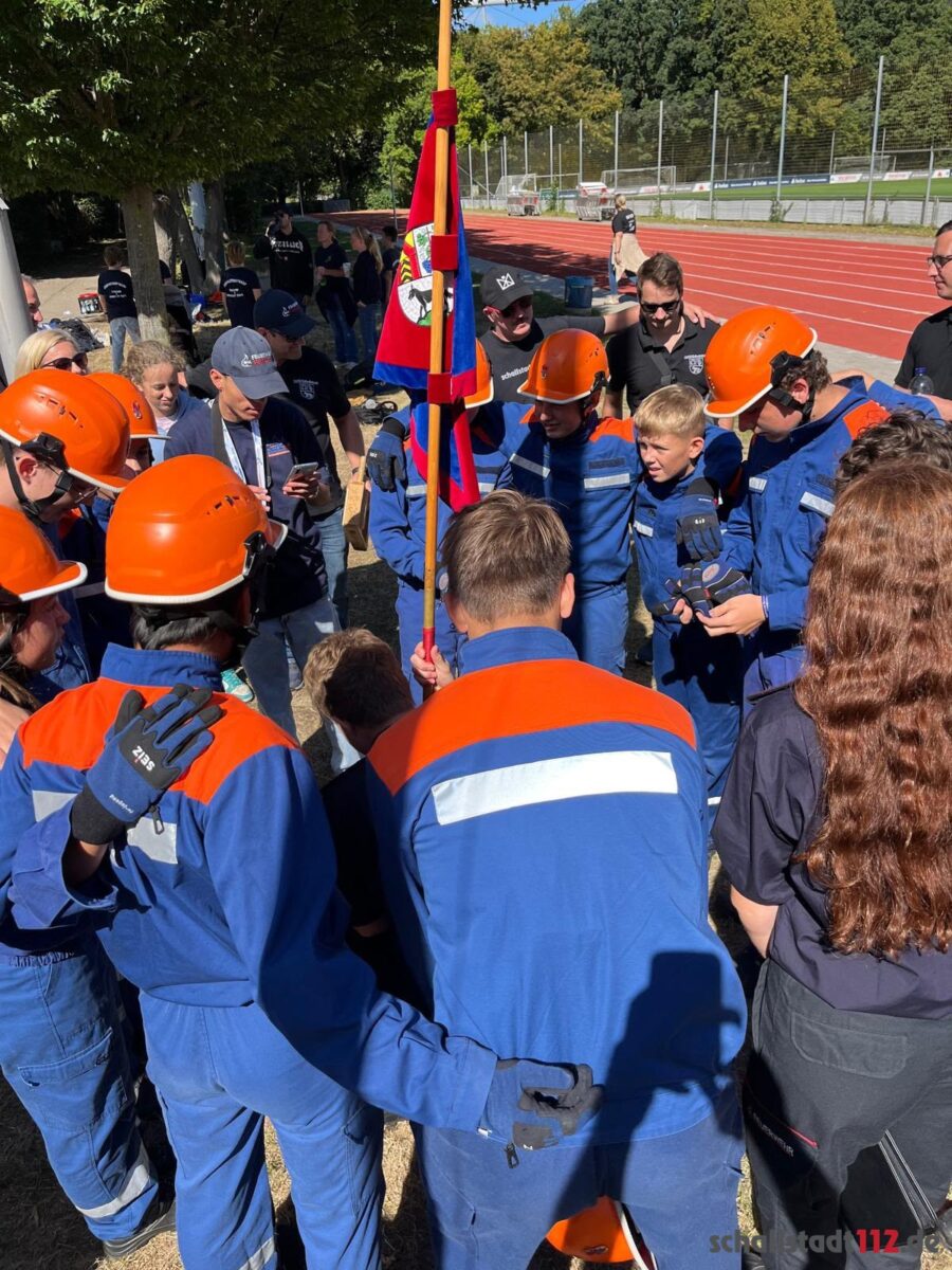 Jugendliche, Betreuer und Unterstützer der Jugendfeuerwehr Schallstadt stehen im Kreis um den Wimpel
